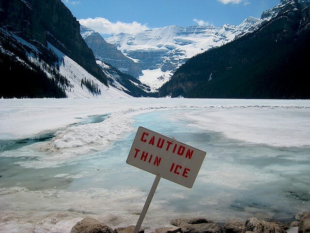 frozen pond by mountain with a sign reading caution thin ice