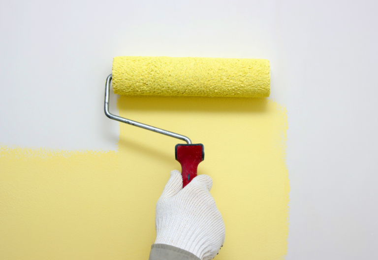 person with white glove painting a white wall with yellow paint