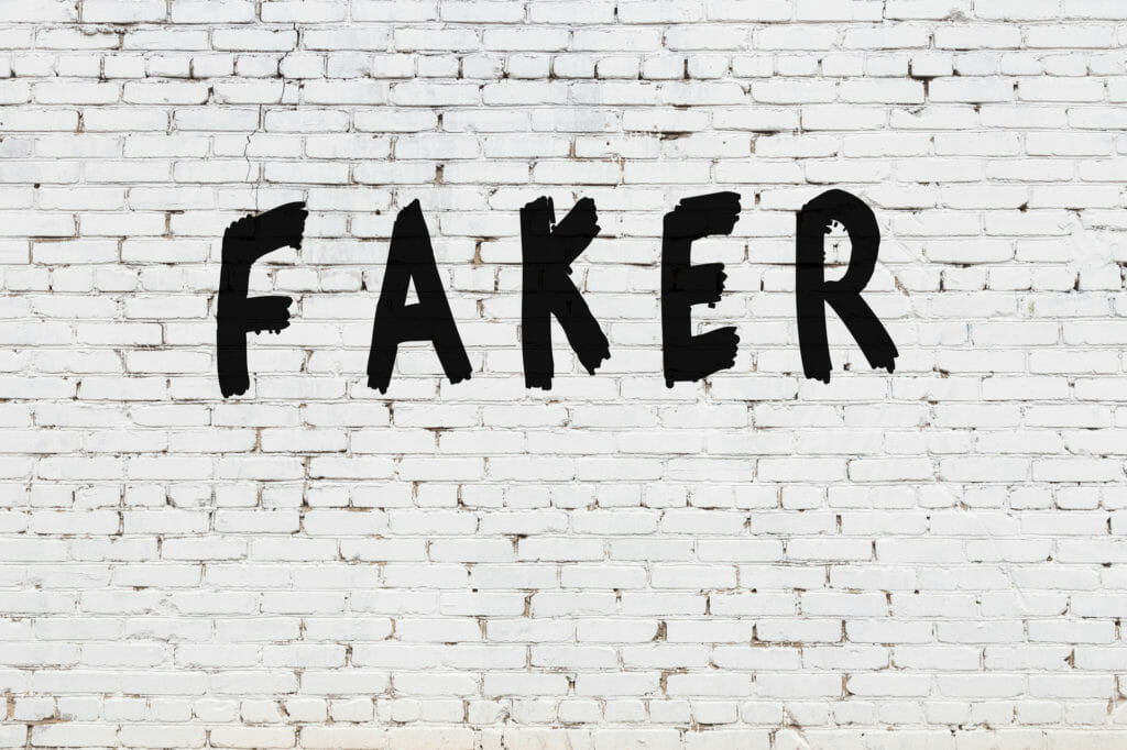Faker scribbled in black paint on white brick wall